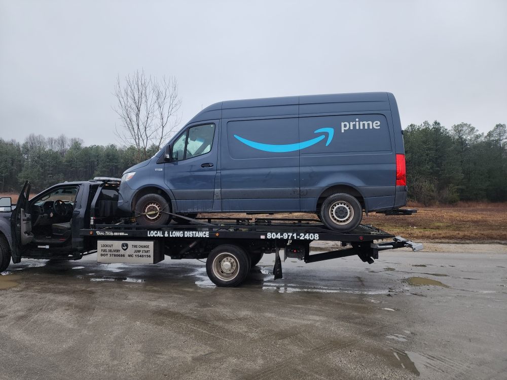 Roadrunner flatbed tow truck loading a disabled van on a wet road