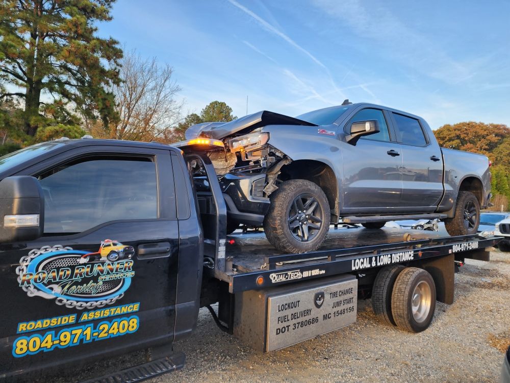 Roadrunner flatbed tow truck hauling a damaged pickup truck